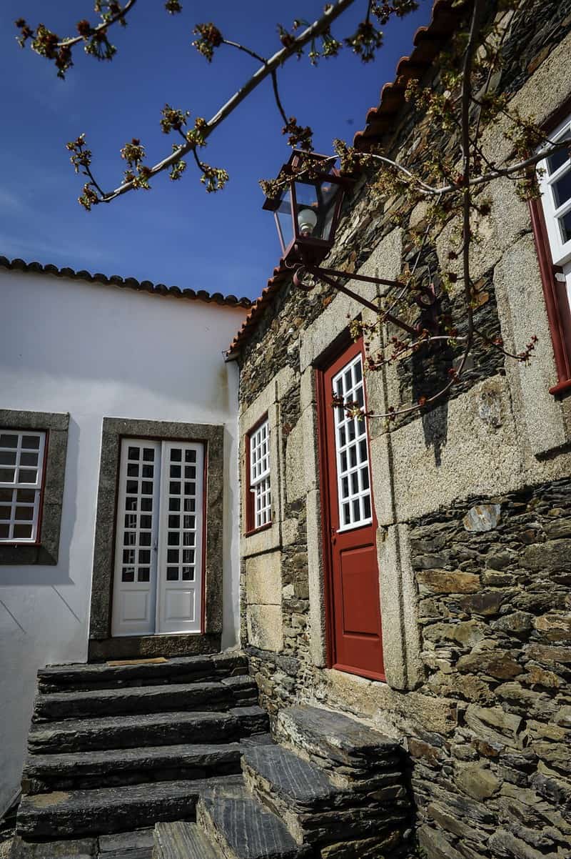 Traditional stone house with red door and white-framed windows in Morgadio da Calçada, Portugal.